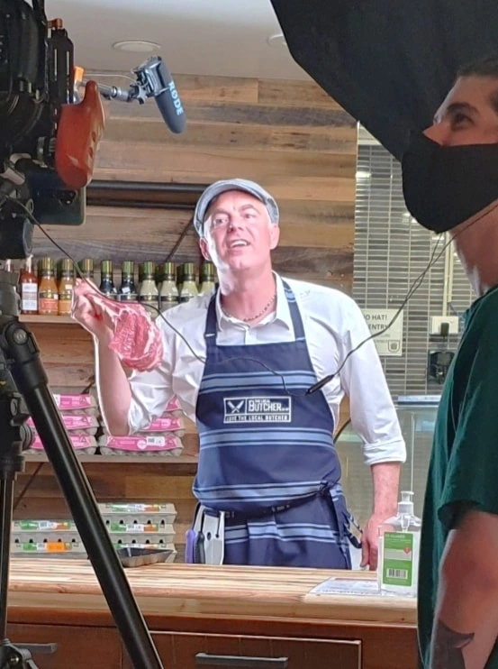 Paul Moore on set filming a national beef commercial, working behind the counter as a butcher under professional studio lights in Geelong.