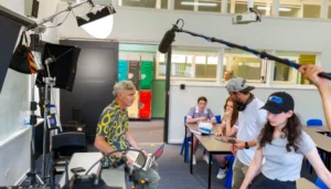 Paul Moore filming a lively classroom discussion scene in Stashamo High, surrounded by students and camera crew.